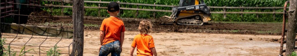 young kids watching skid steer on farm
